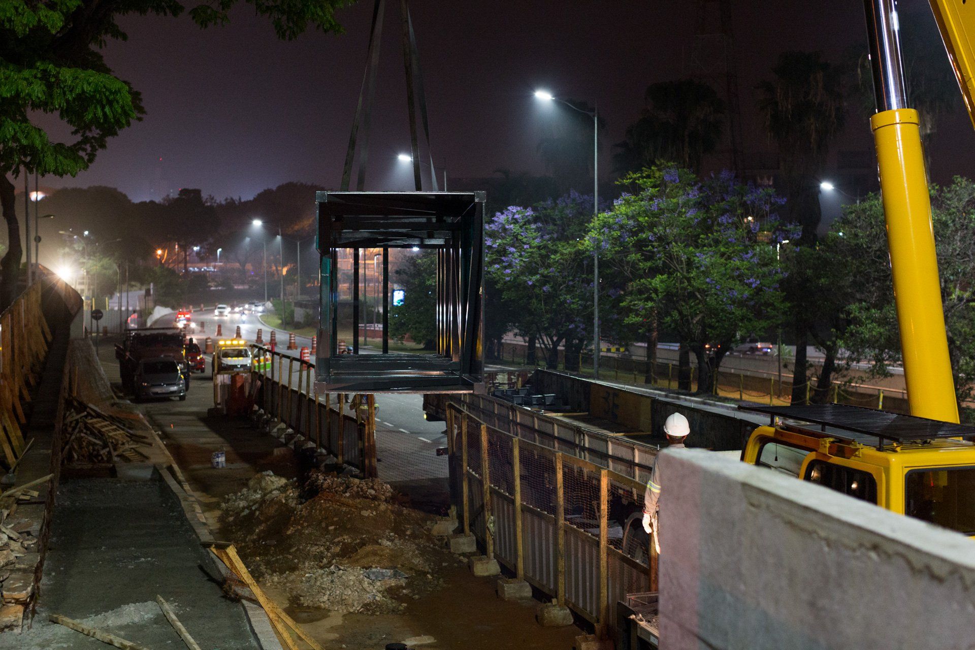 Um canteiro de obras à noite com um guindaste levantando um contêiner.