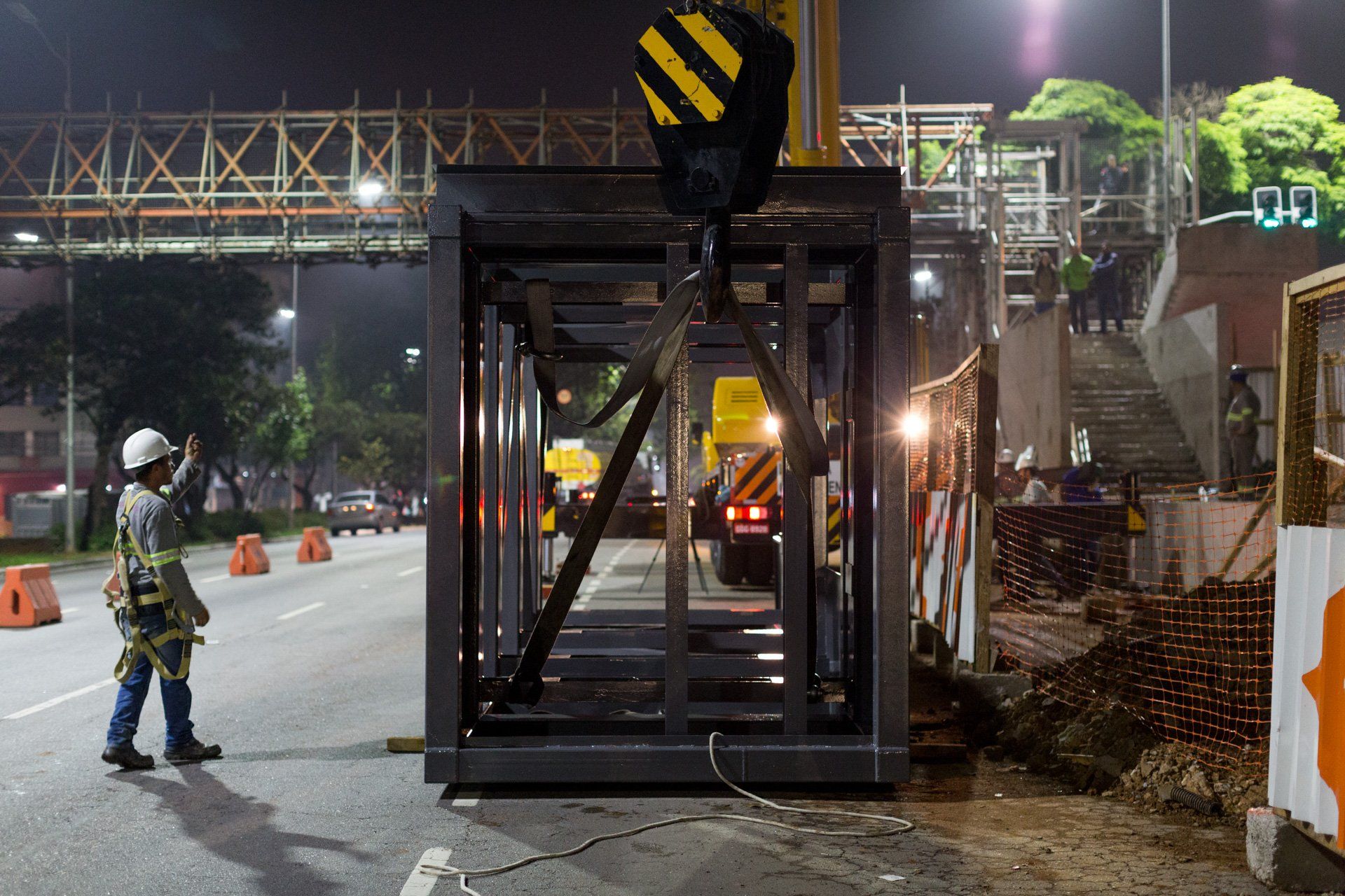 Um trabalhador da construção civil está parado ao lado de um guindaste na beira da estrada.