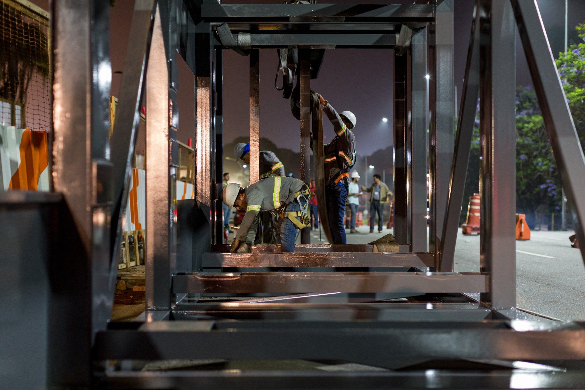 Um grupo de trabalhadores da construção civil trabalha em uma estrutura metálica à noite.