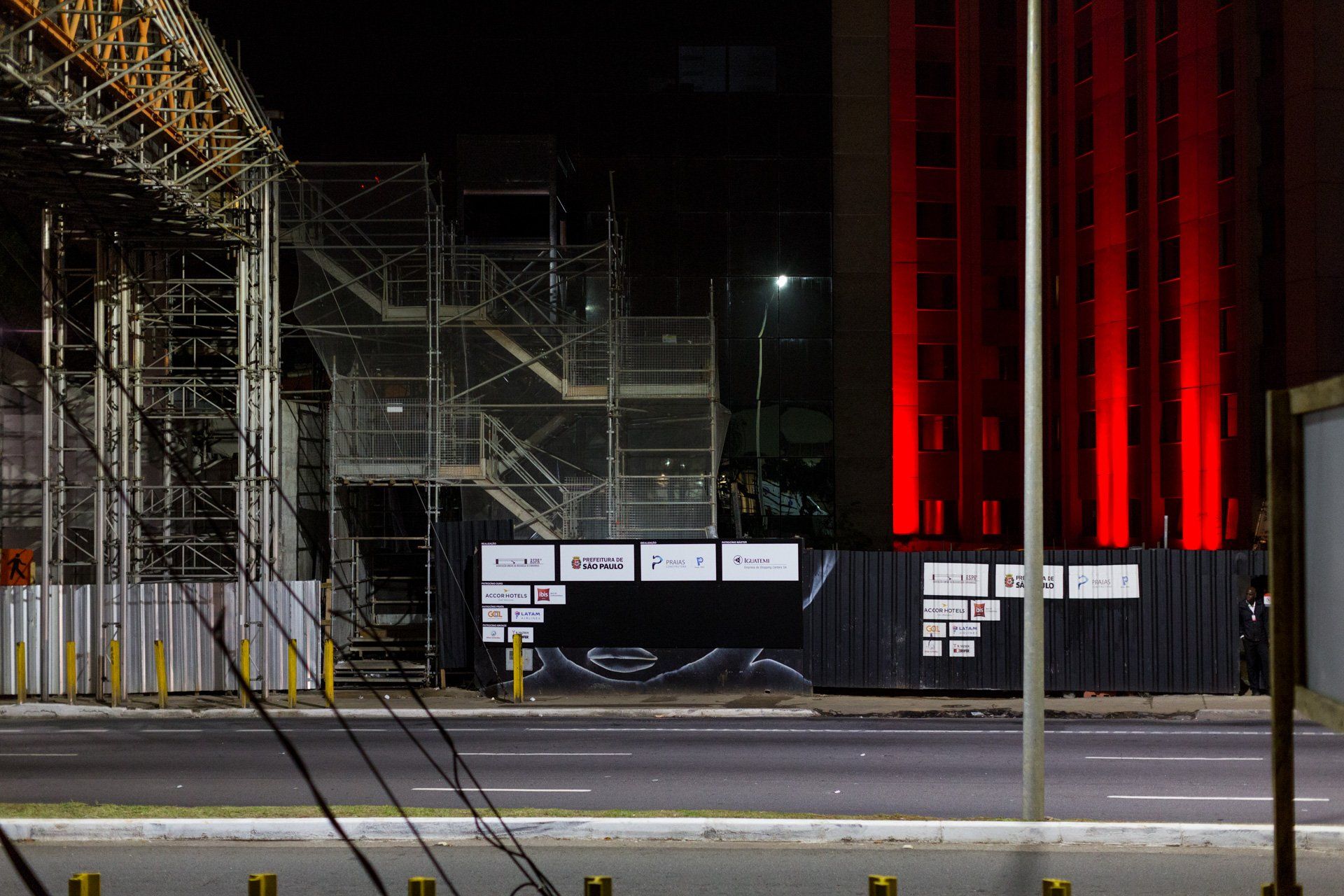 Um prédio em construção fica iluminado em vermelho à noite.