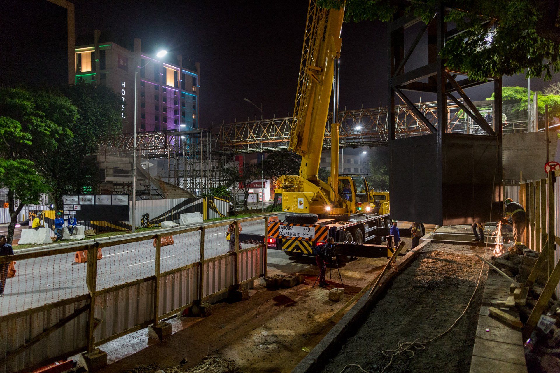 Um canteiro de obras à noite com um grande guindaste amarelo.