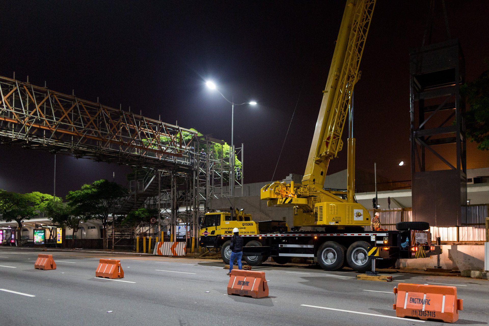 Um grande guindaste amarelo está parado na beira de uma estrada à noite.