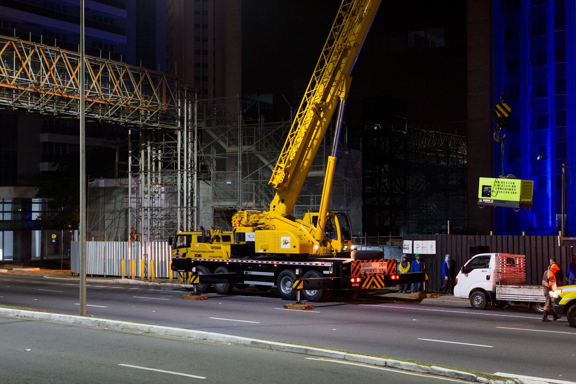 Um grande guindaste amarelo está estacionado na beira da estrada à noite.