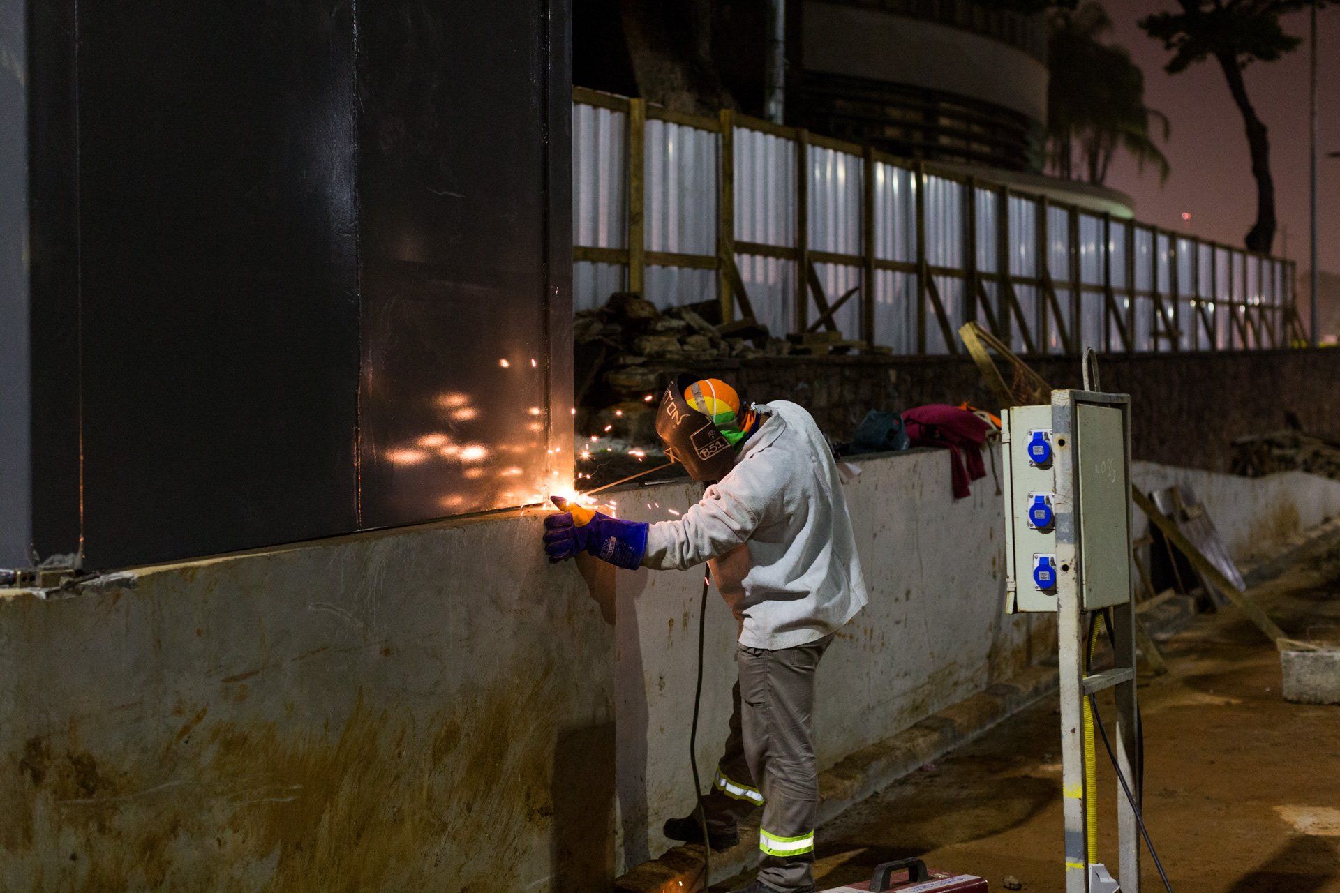 Um homem está soldando uma parede de metal à noite.