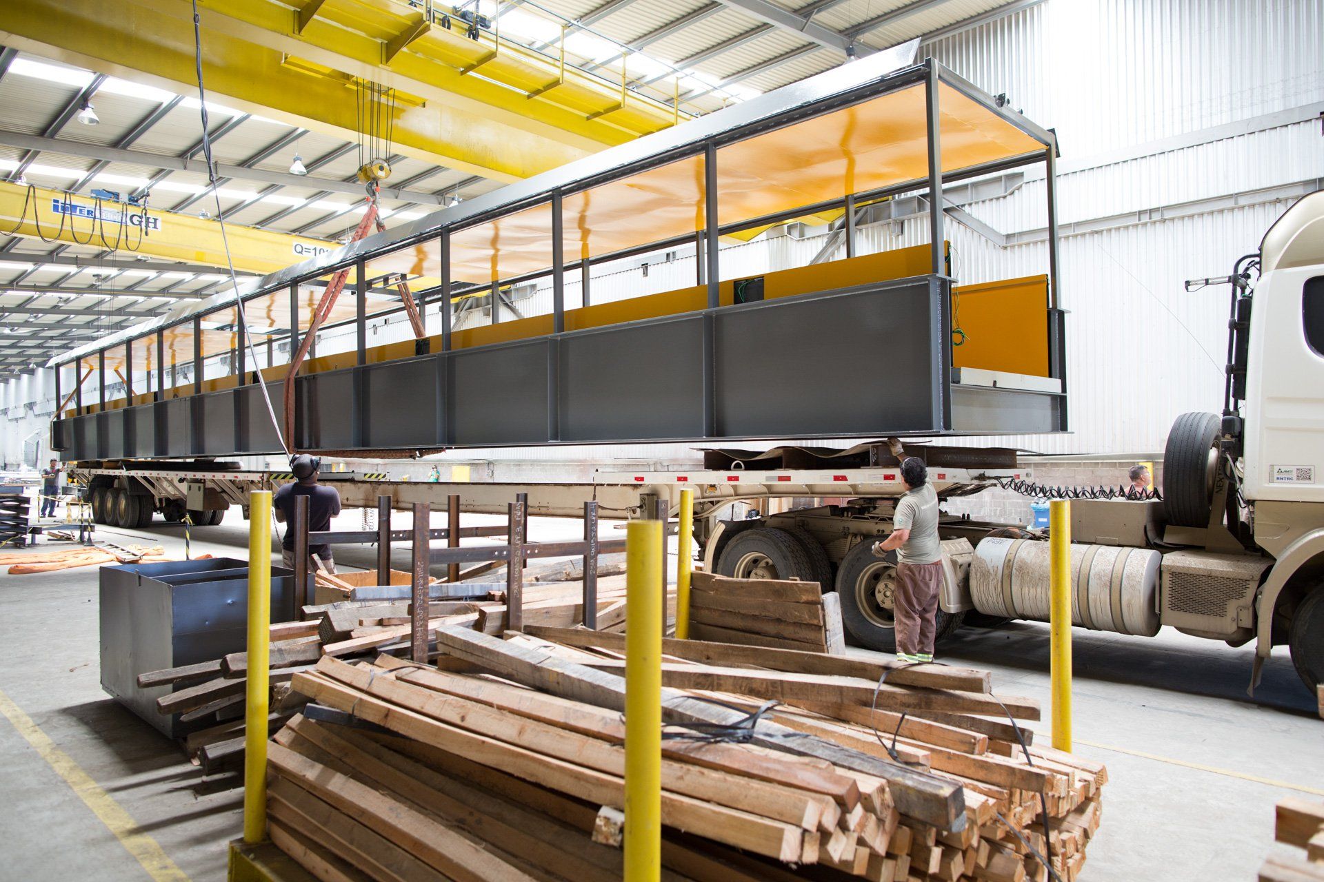 Um caminhão está parado em um armazém próximo a uma pilha de madeira.