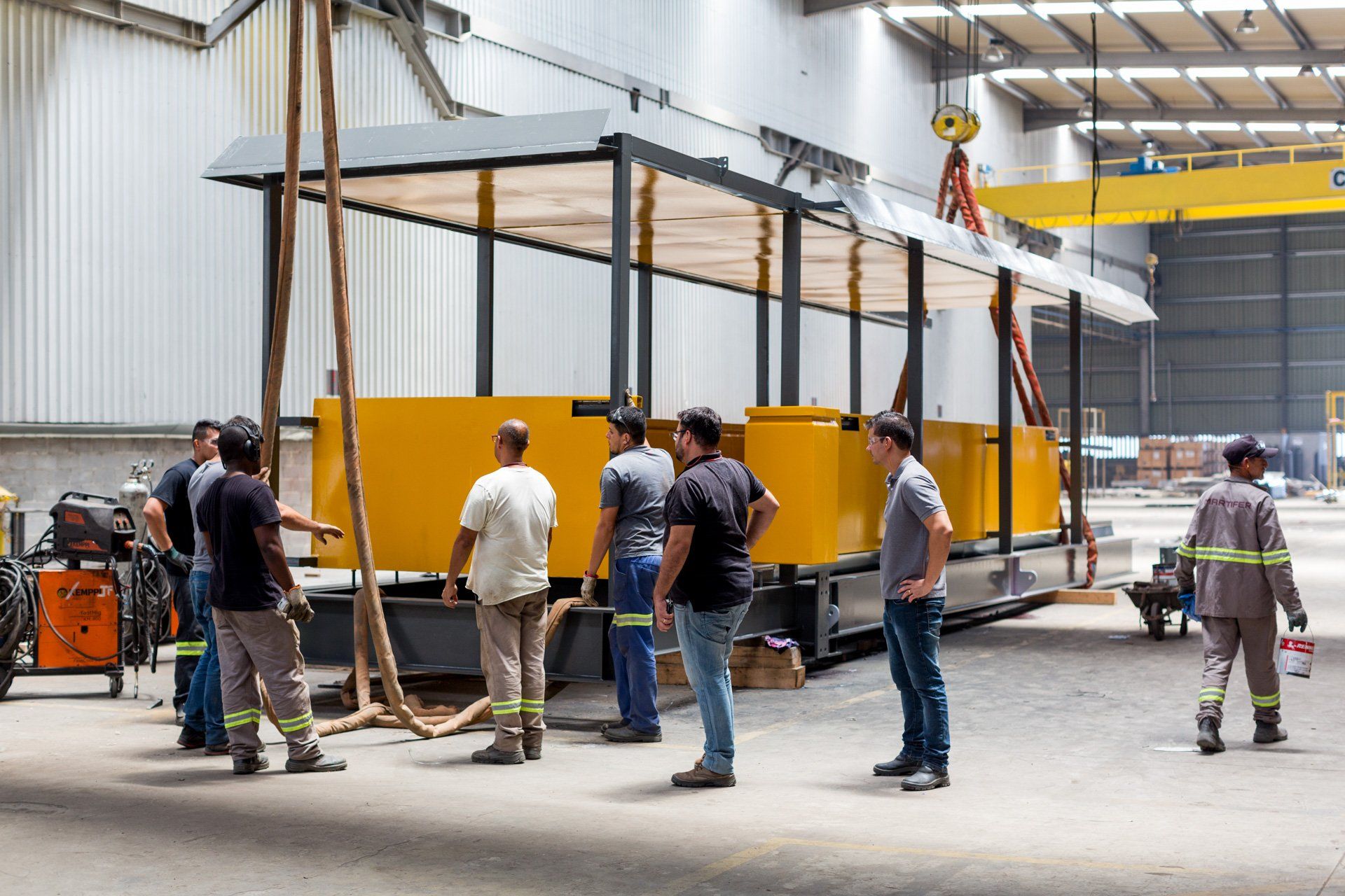 Um grupo de homens está em volta de um prédio amarelo de uma fábrica.