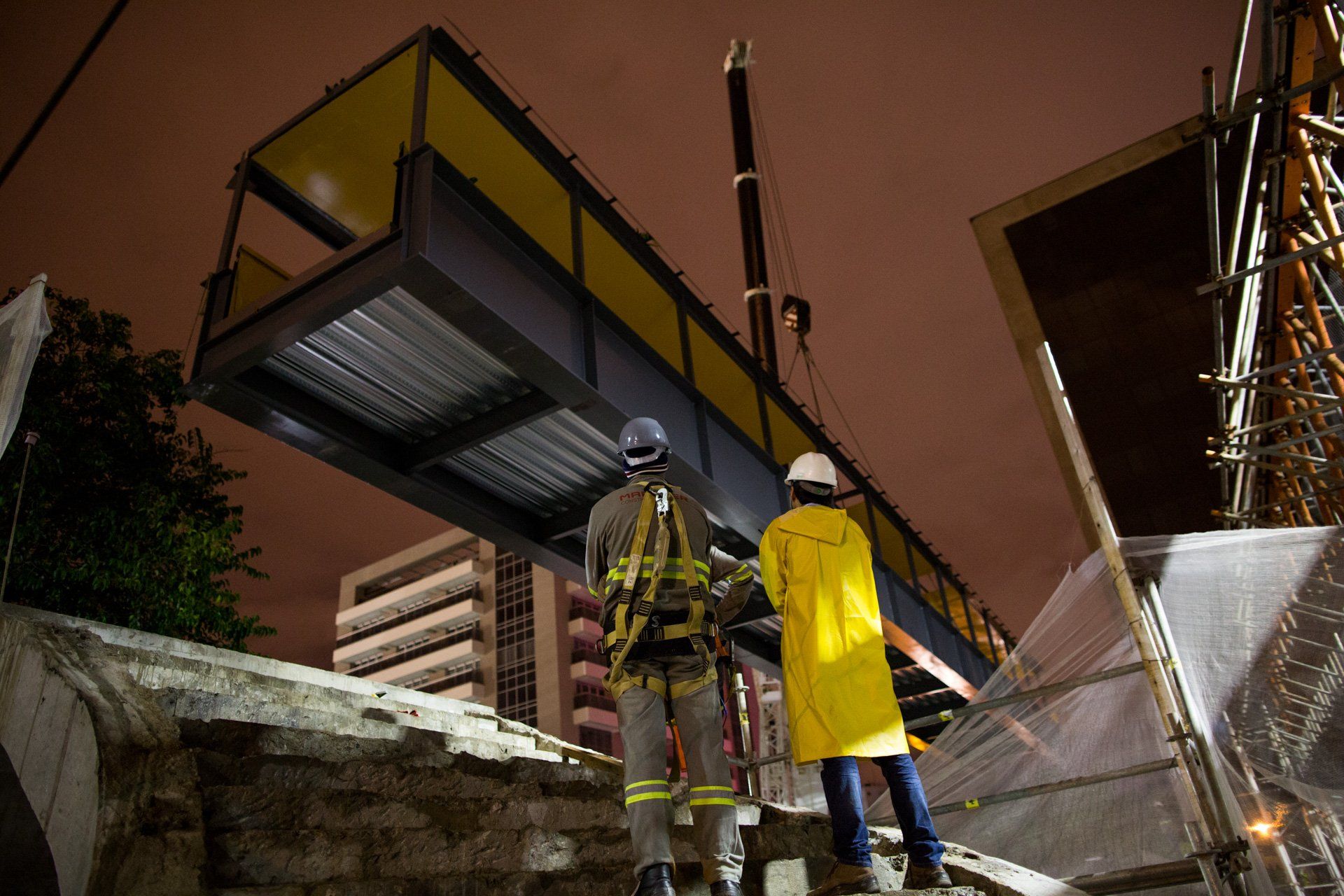 Dois trabalhadores da construção civil estão trabalhando em uma ponte à noite.