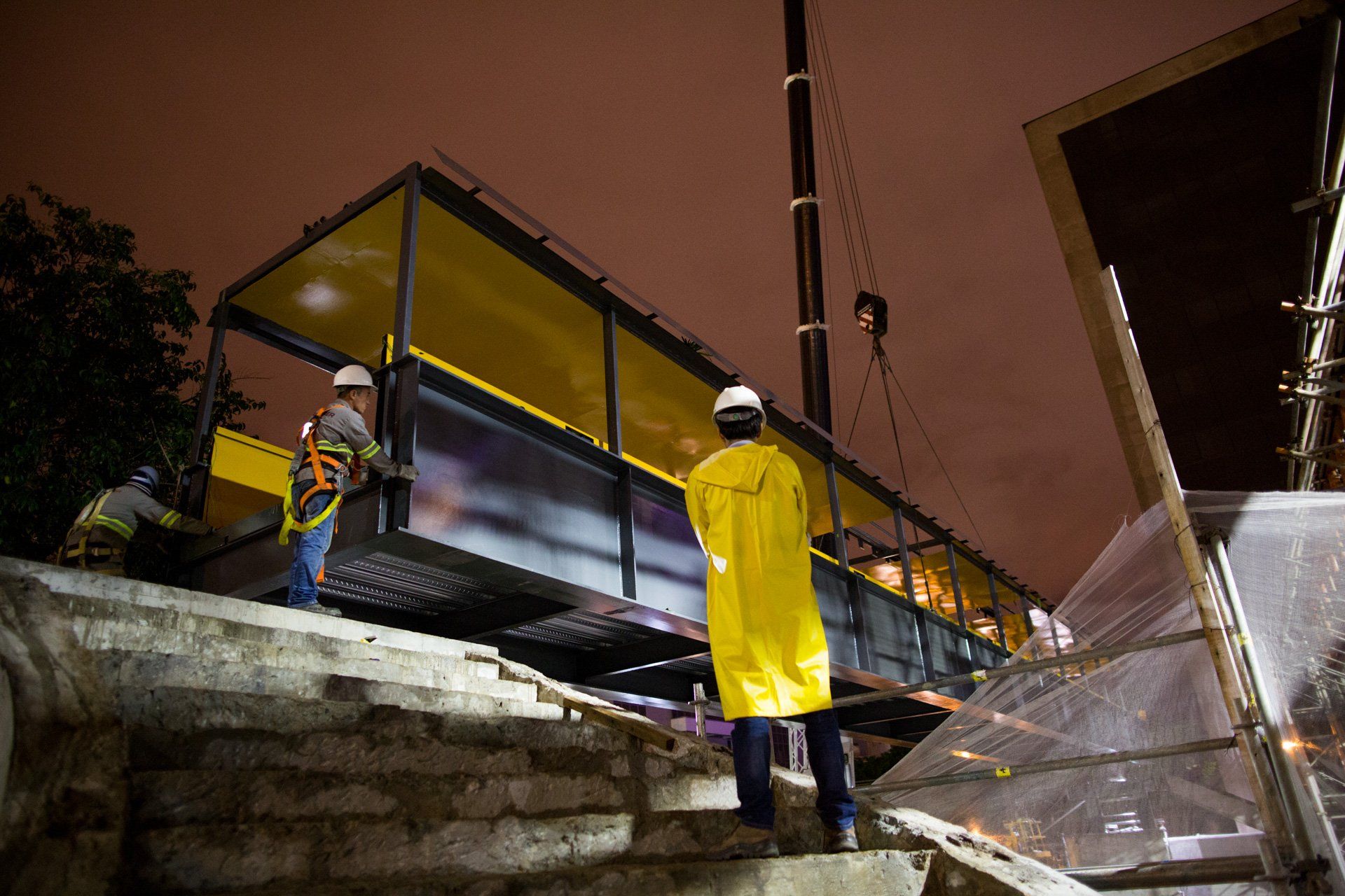 Um grupo de trabalhadores da construção civil trabalha em uma ponte à noite.