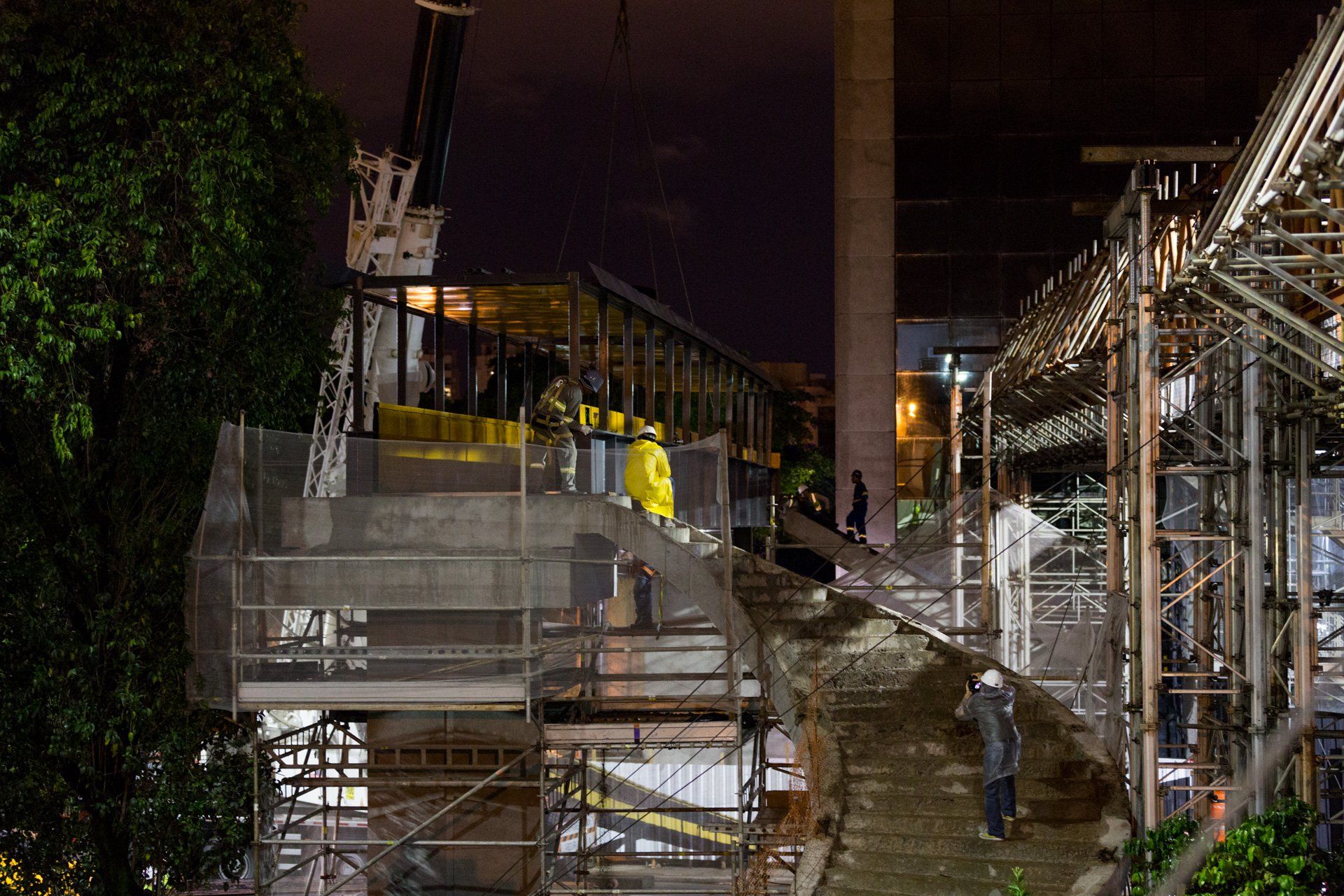Um grupo de trabalhadores da construção civil trabalha em uma ponte à noite.