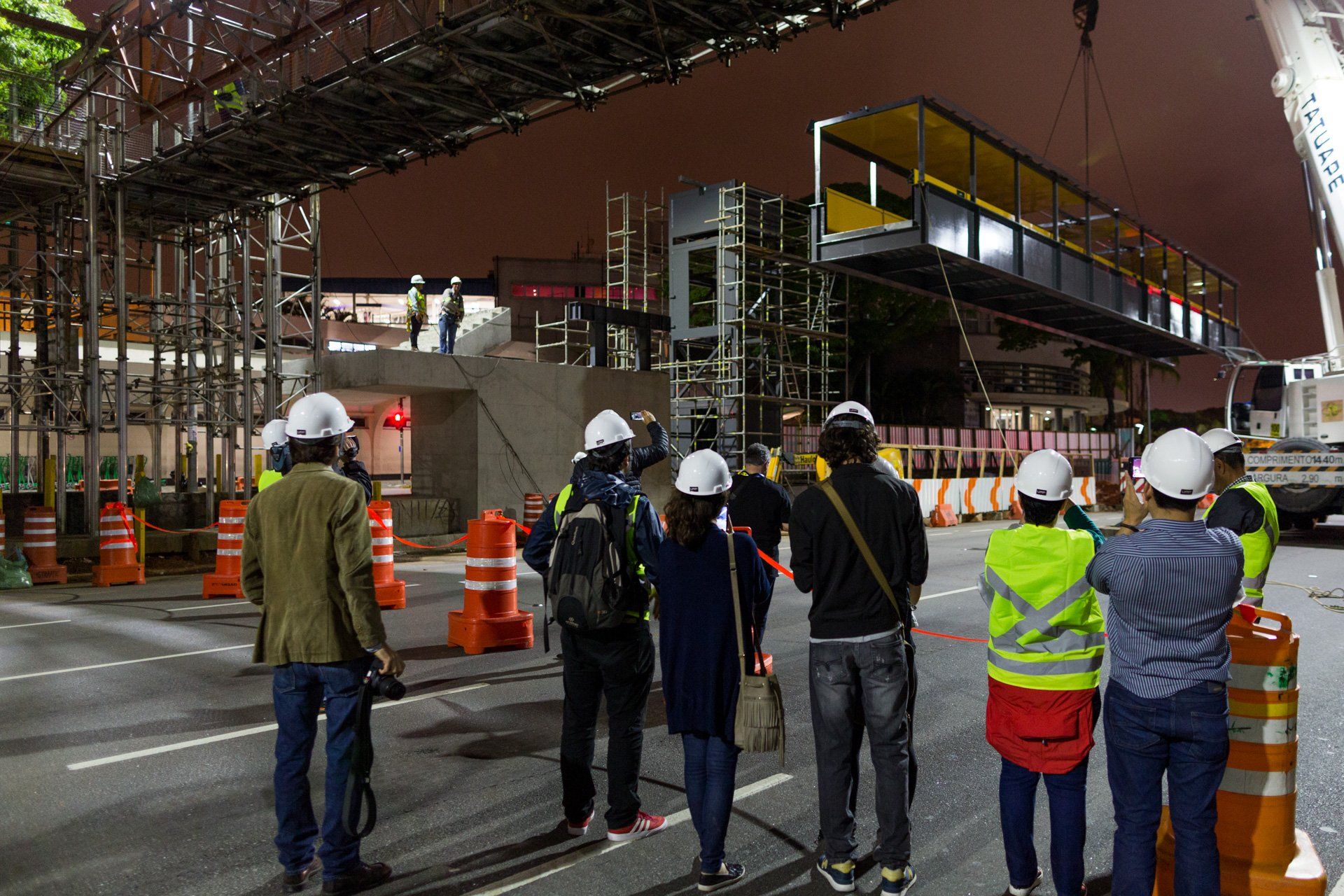 Um grupo de pessoas está em frente a um canteiro de obras à noite.