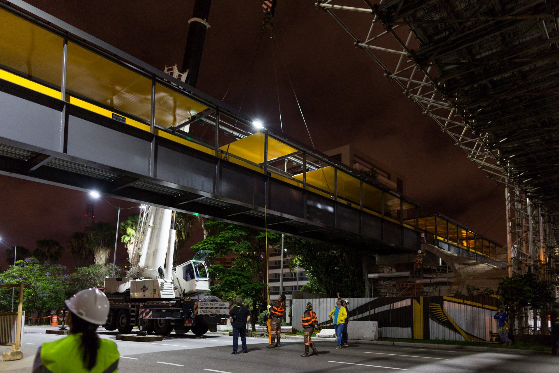 Um grupo de trabalhadores da construção civil trabalha em uma ponte à noite.