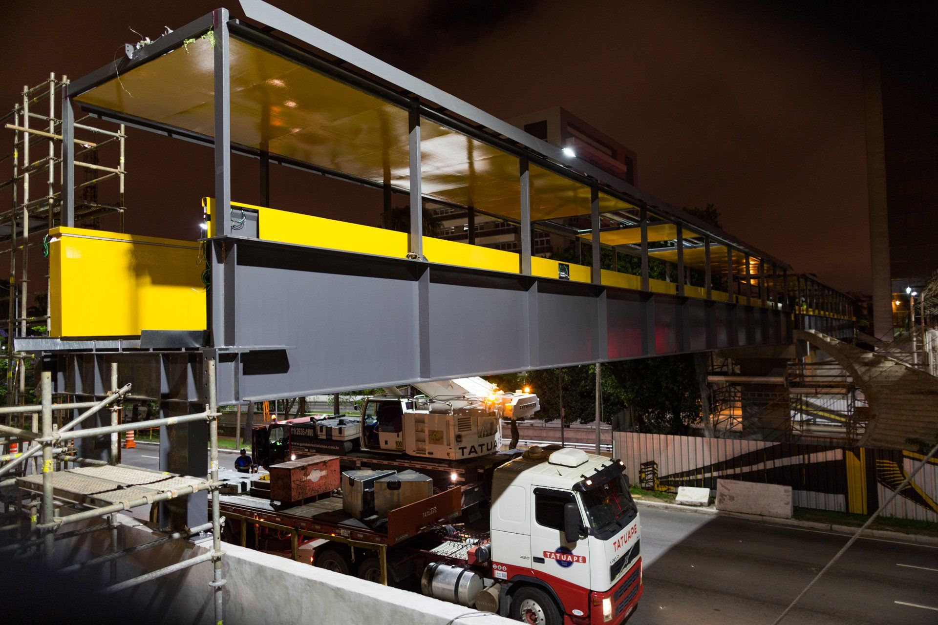 Um caminhão transporta uma ponte em construção à noite.