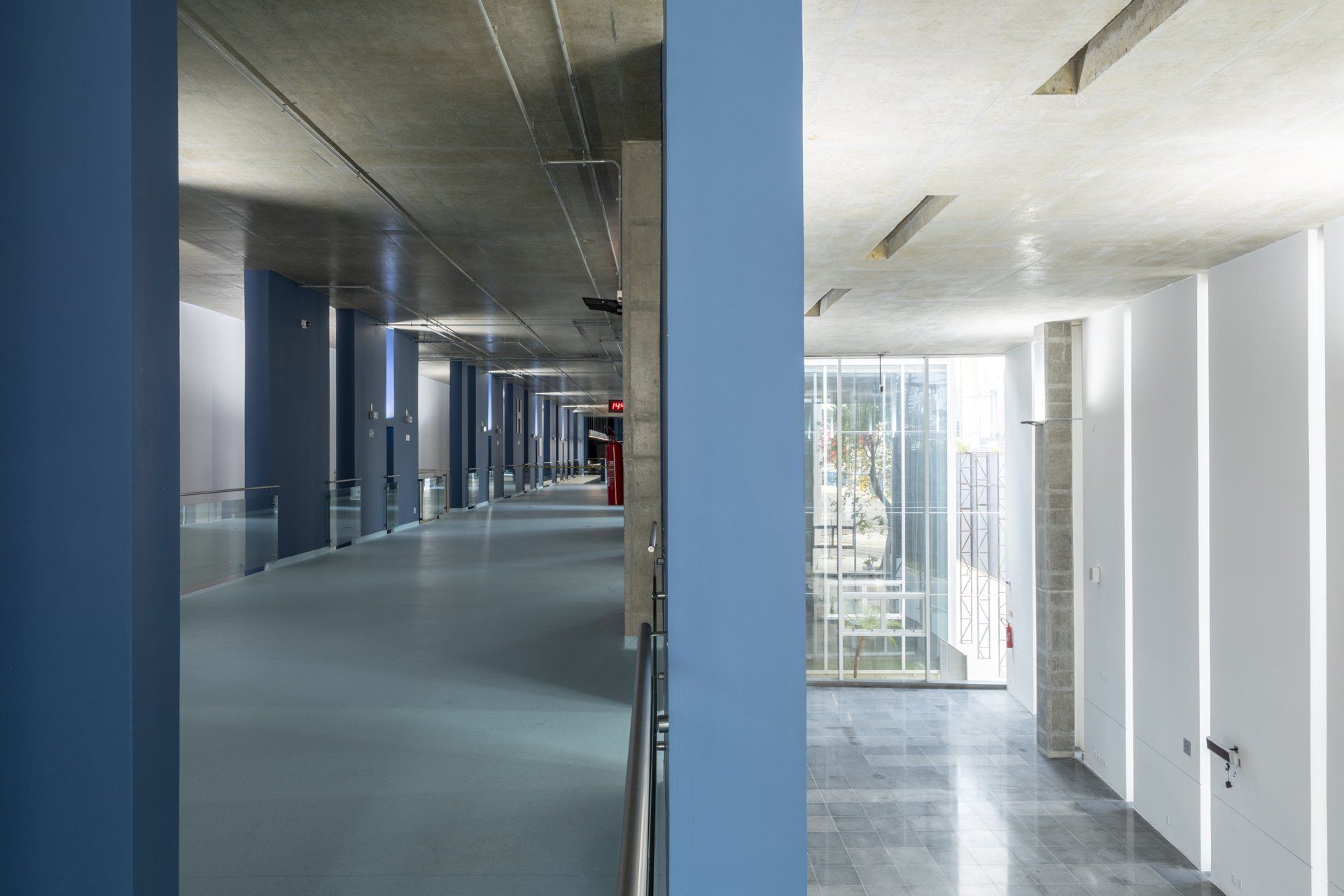Um longo corredor em um prédio com paredes azuis e portas brancas.