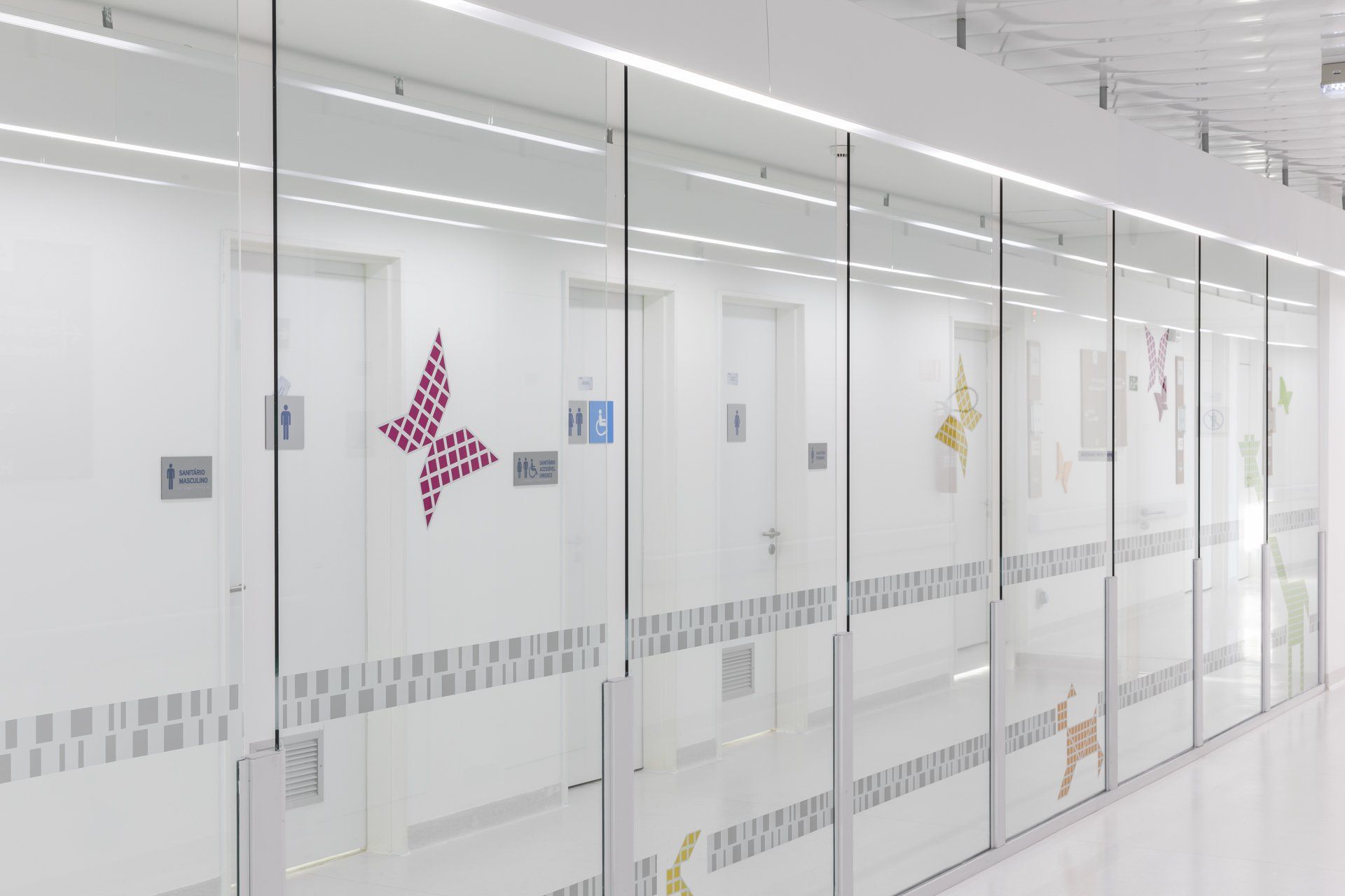 Um longo corredor com portas de vidro e uma borboleta na parede.