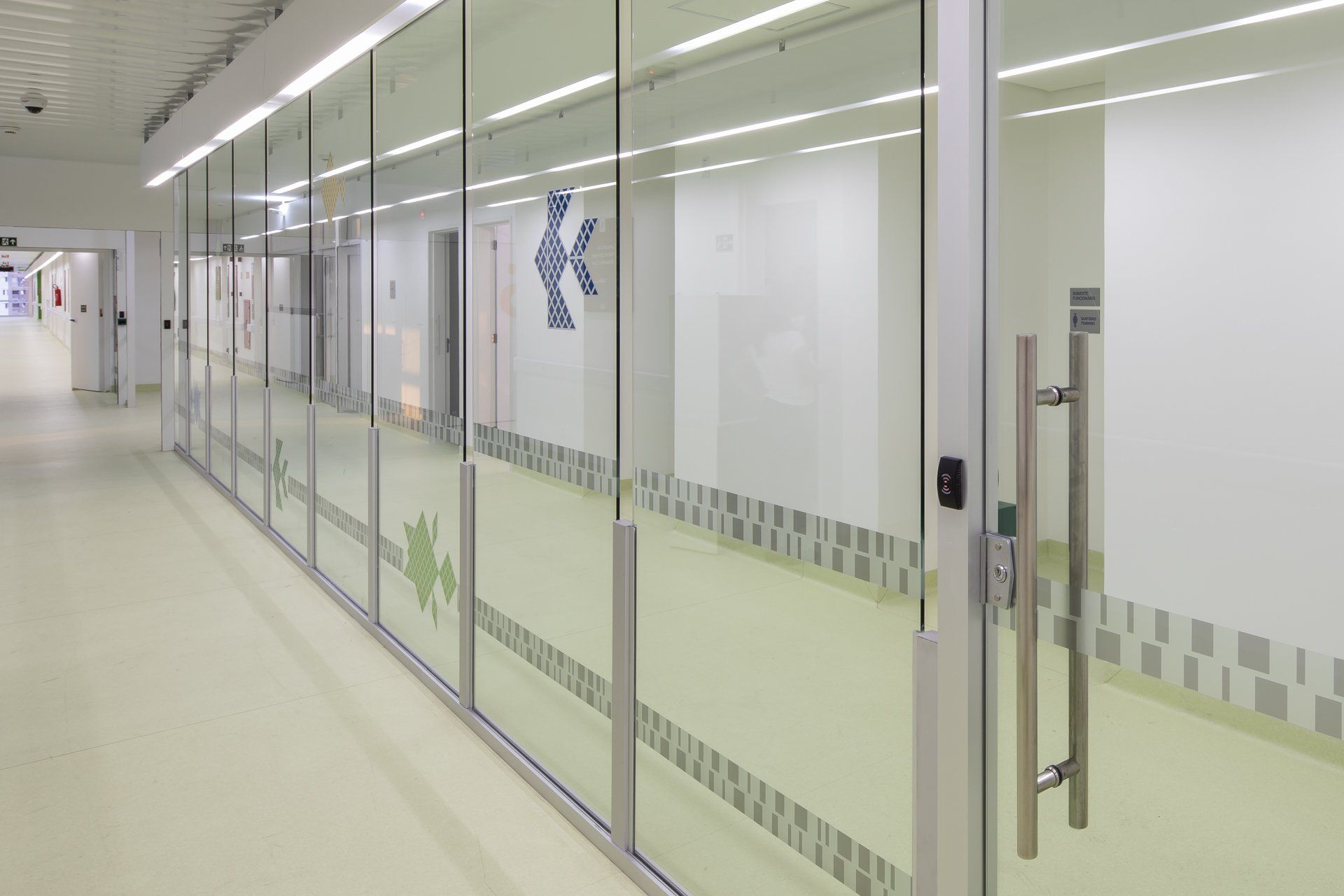 Um longo corredor com paredes e portas de vidro em um hospital.