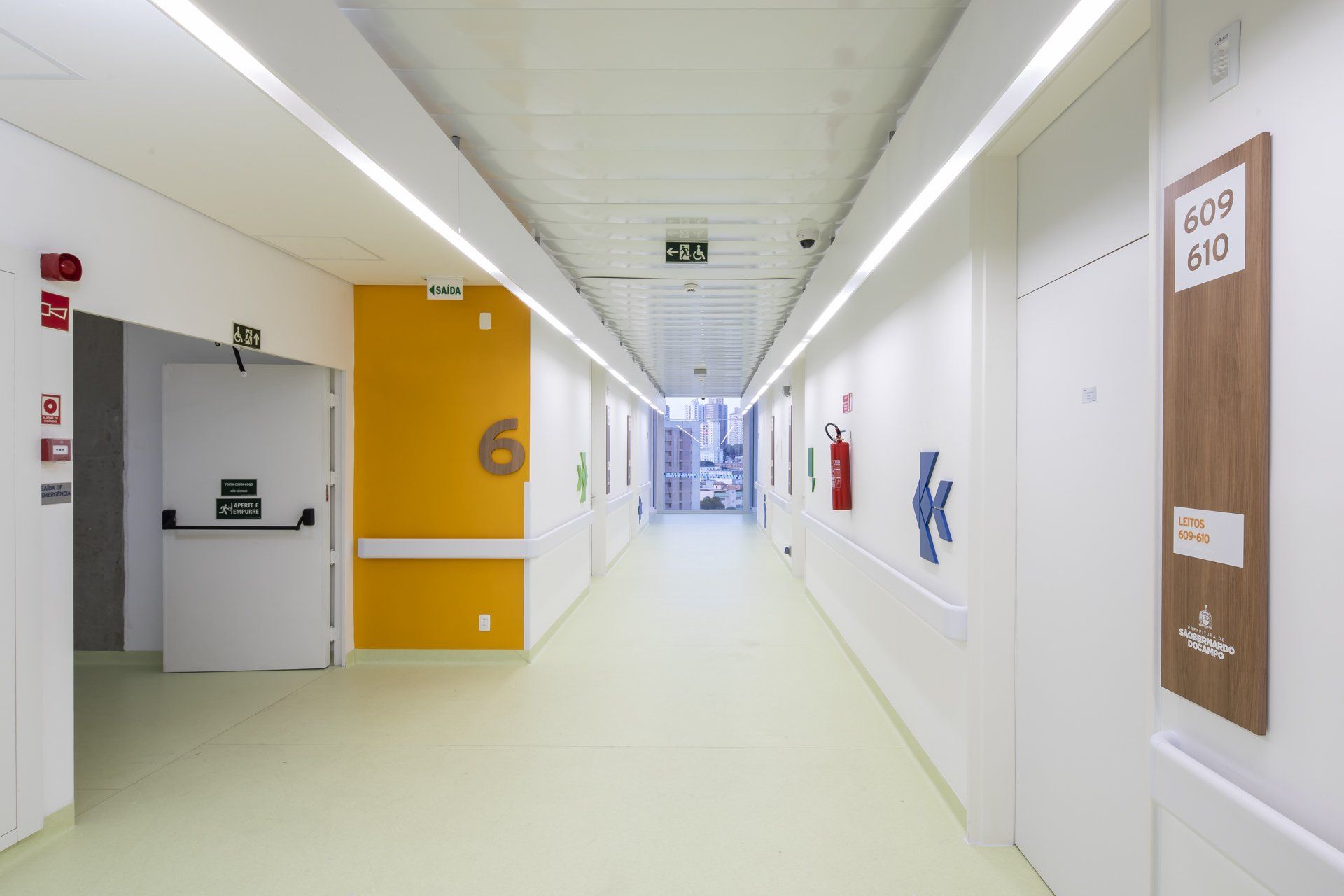 Um longo corredor de um hospital com paredes amarelas e piso verde.