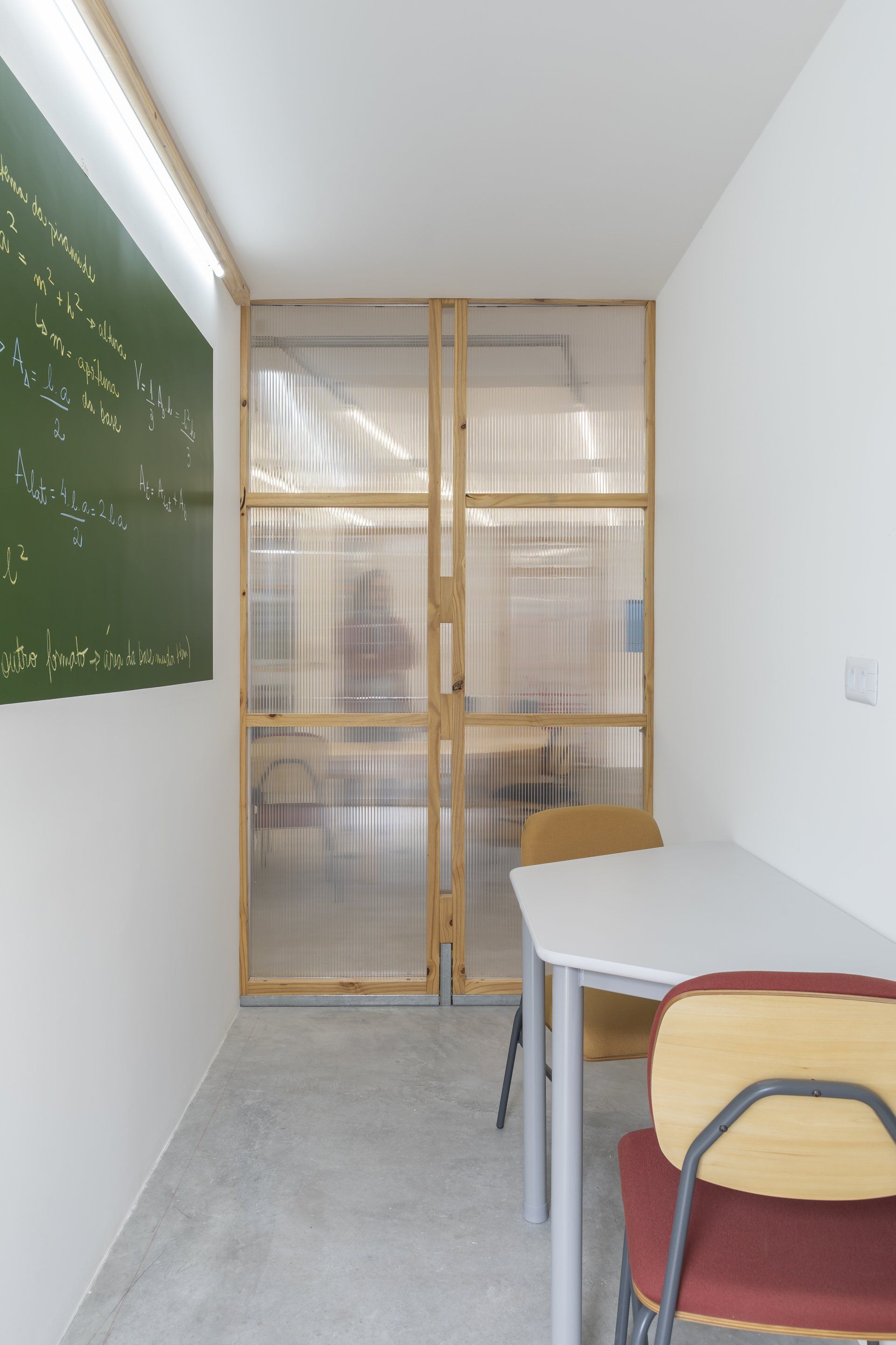 Uma sala de aula com mesa e cadeiras e um quadro verde na parede