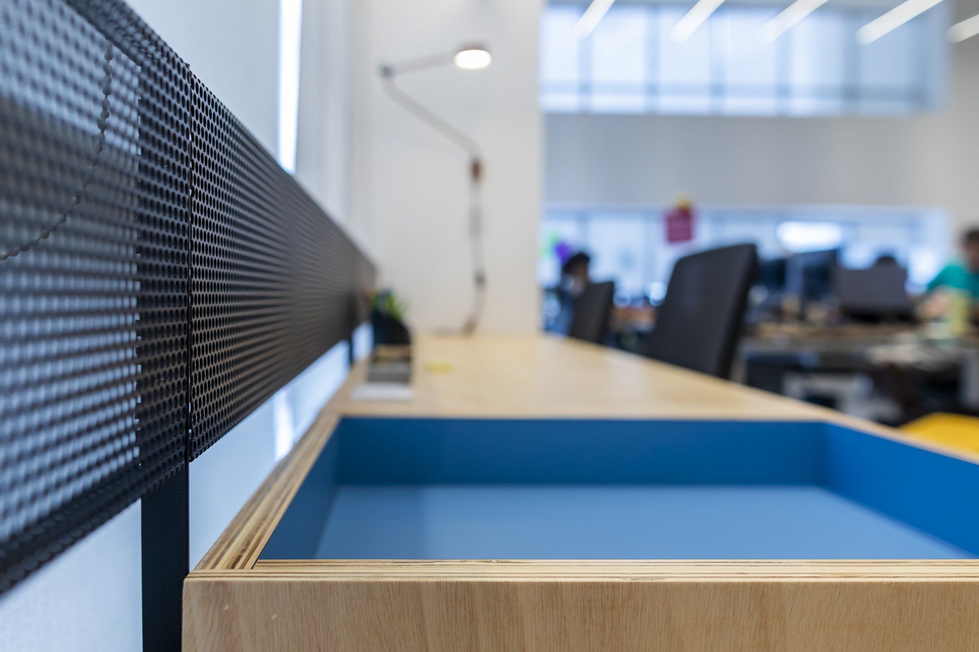 Uma mesa de madeira com uma bandeja azul embaixo em um escritório.