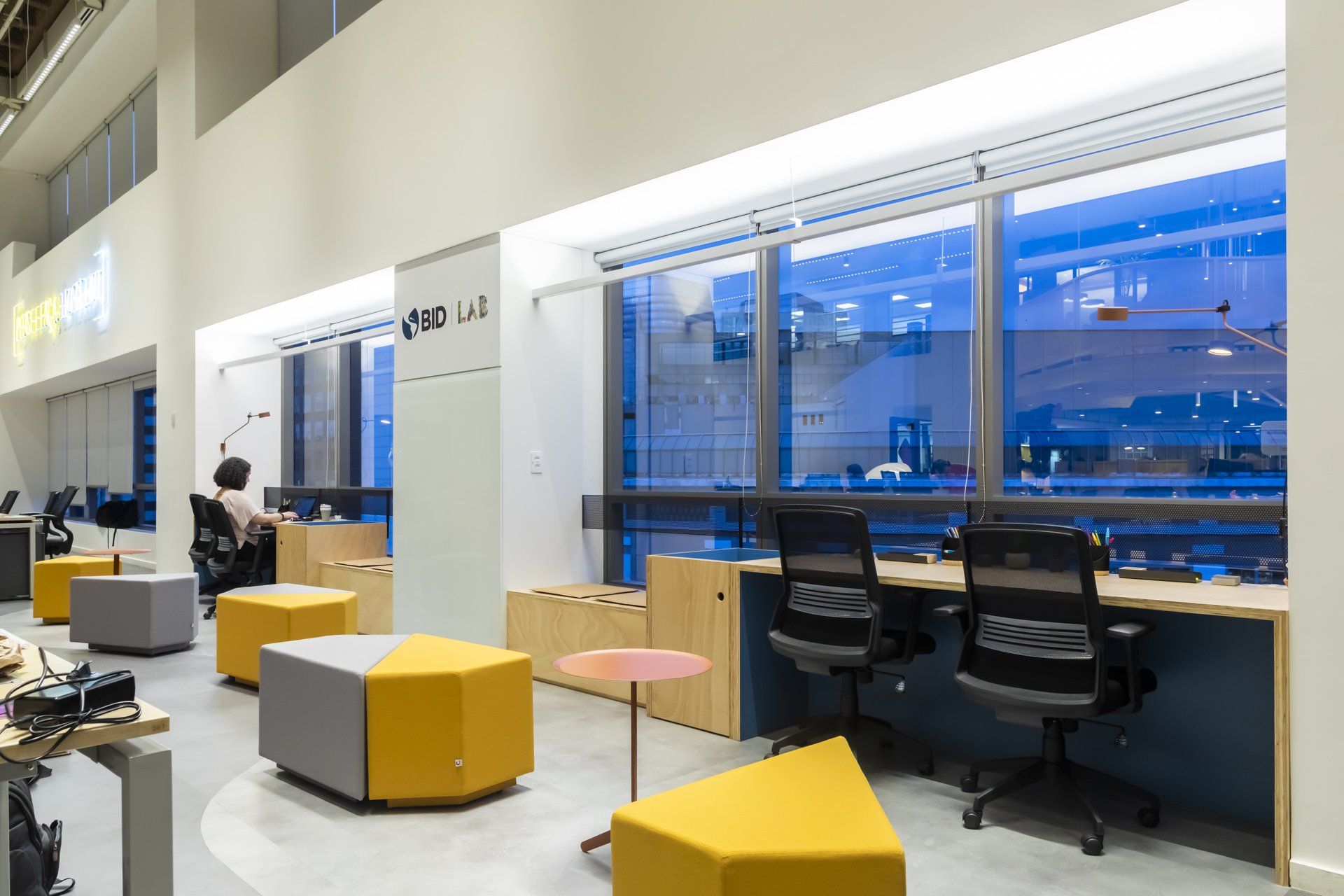 Um homem está sentado em uma mesa em um escritório com muitas janelas.