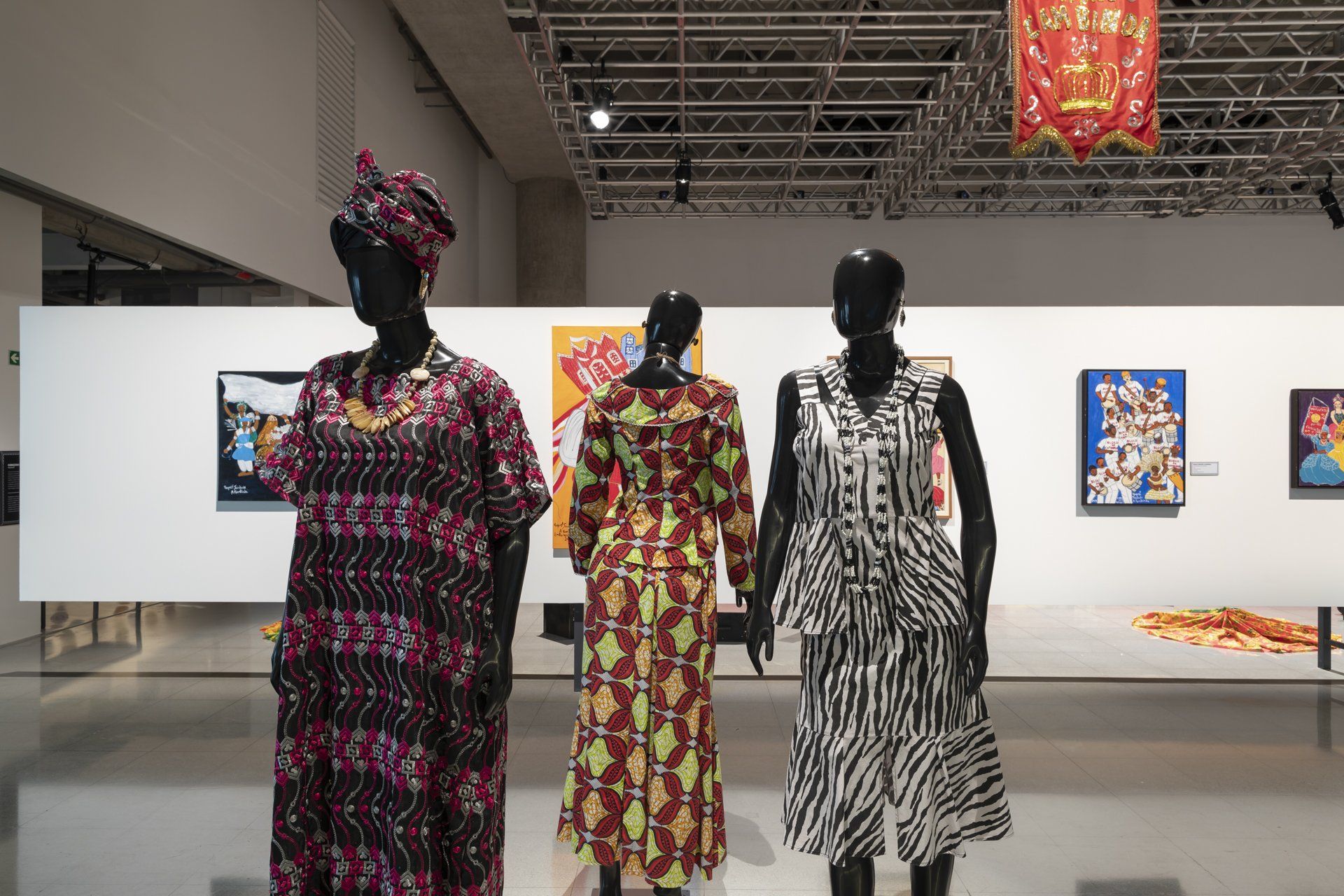 Três manequins usando vestidos estão lado a lado em um museu.