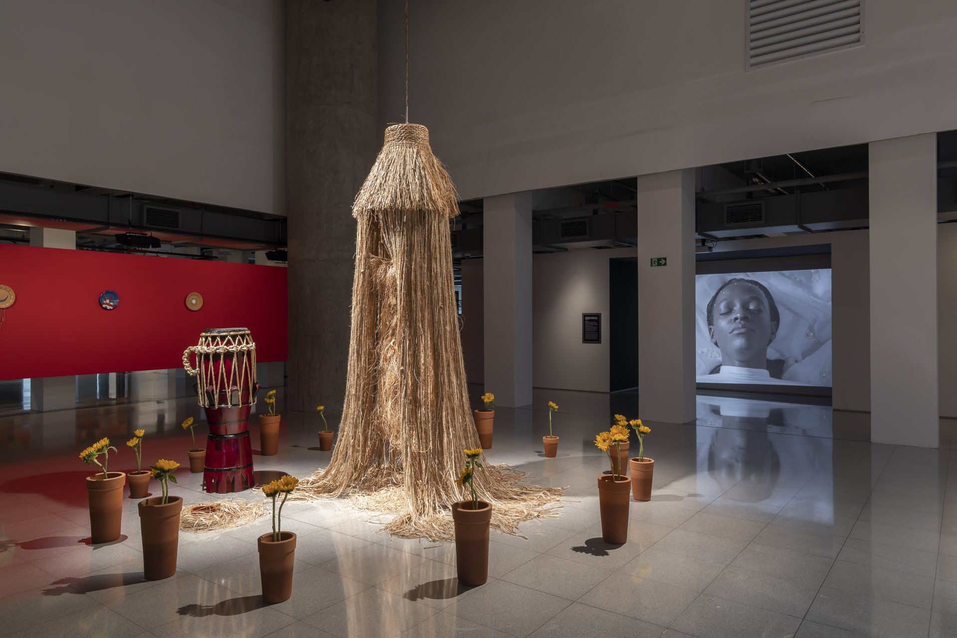 Há uma grande escultura no meio da sala cercada por vasos de plantas.