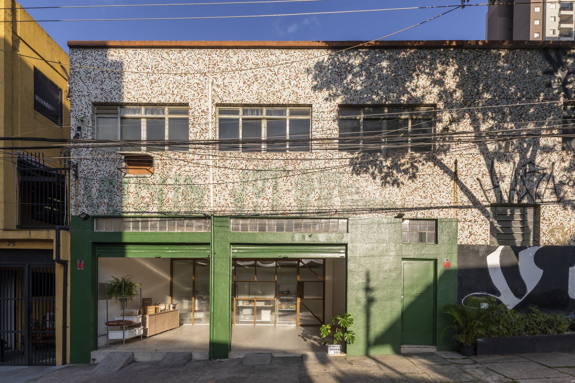 A frente de um prédio com uma porta verde e um prédio amarelo ao fundo.