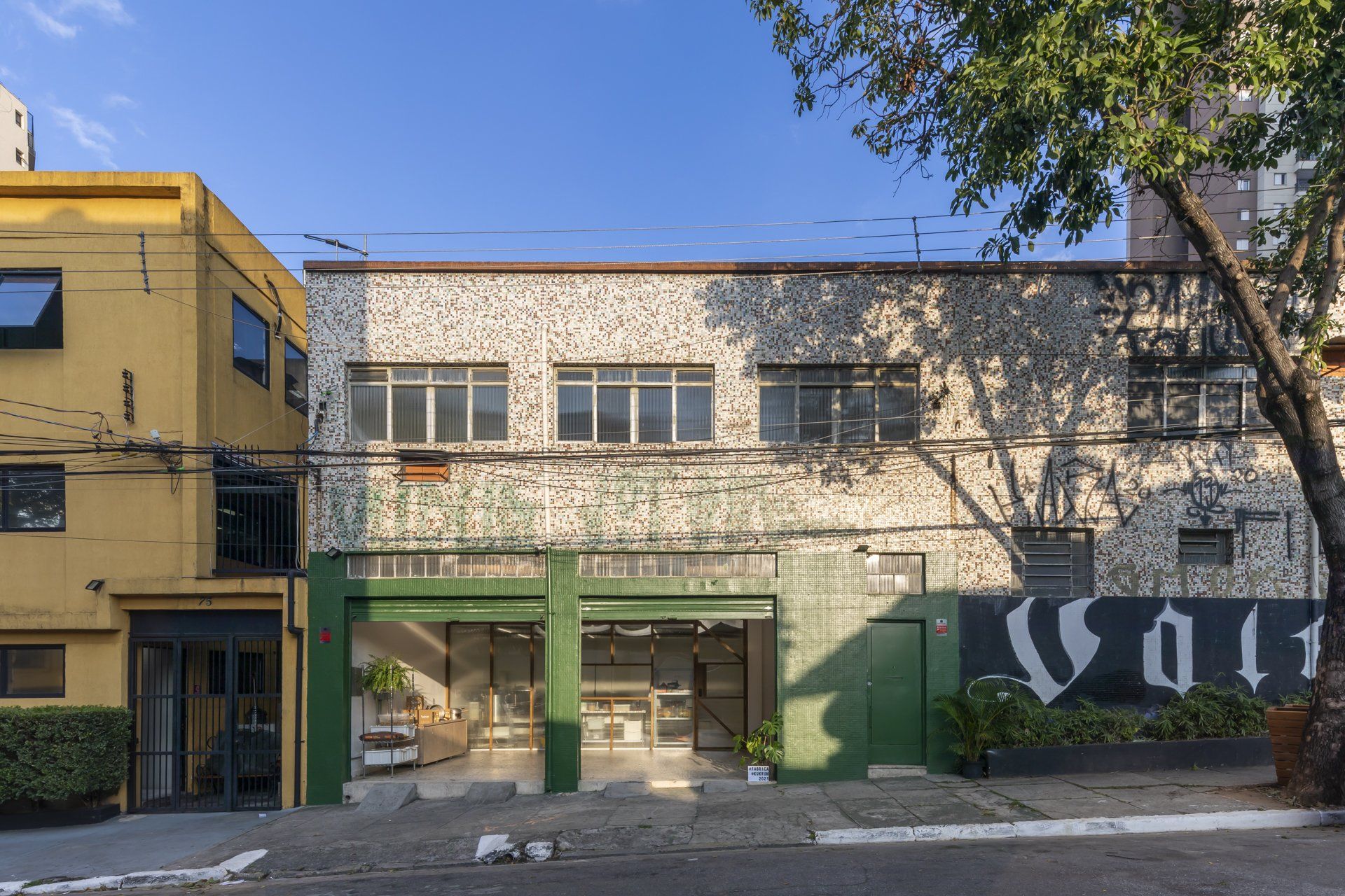 Um grande prédio com uma porta verde e um prédio amarelo ao fundo.