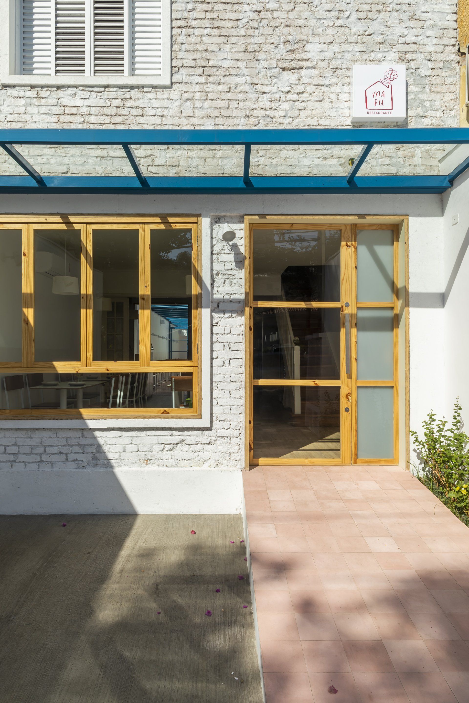 Um prédio de tijolos brancos com porta de vidro e cobertura azul.