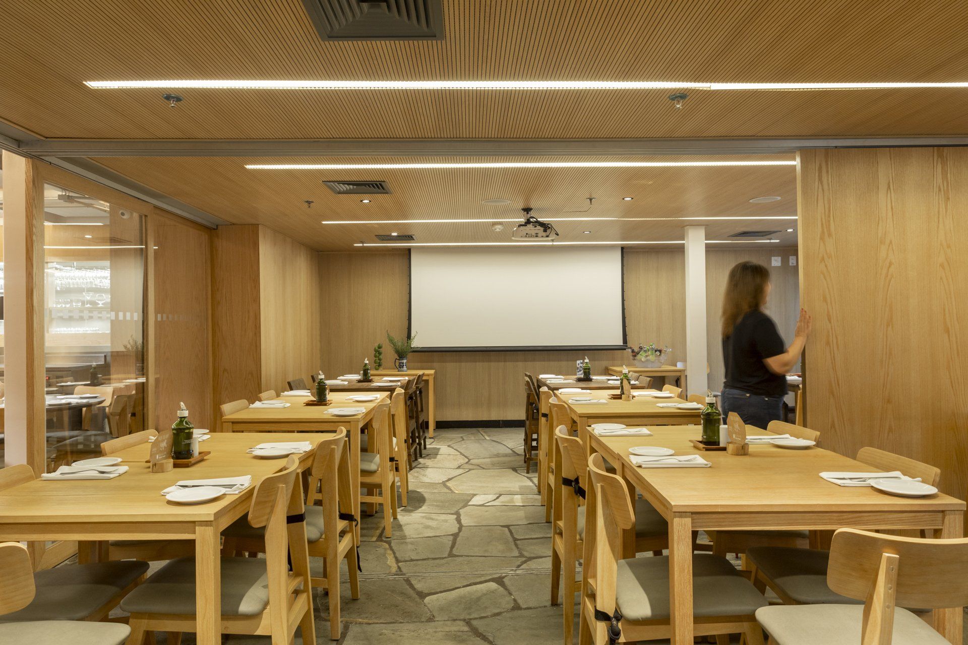 Um restaurante com mesas e cadeiras e tela de projeção.