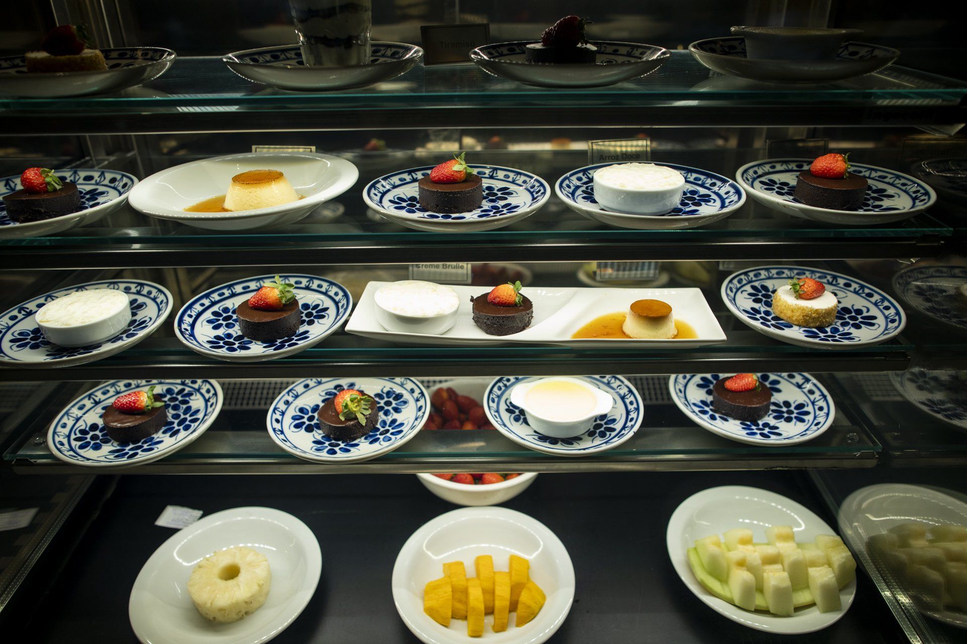 Uma vitrine repleta de pratos de sobremesas e frutas.