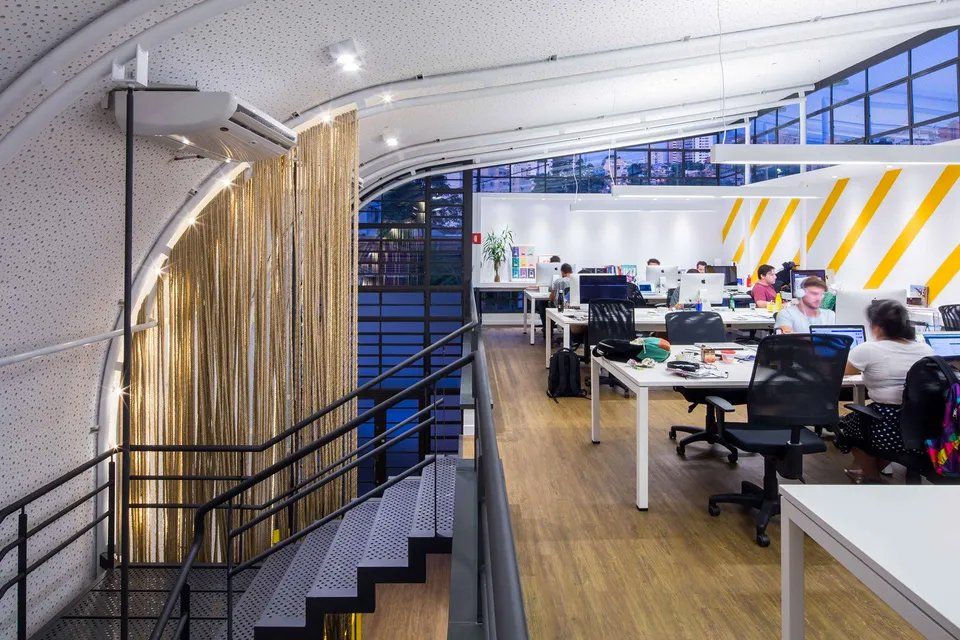 Um grande escritório com mesas e cadeiras e escadas que levam ao segundo andar.