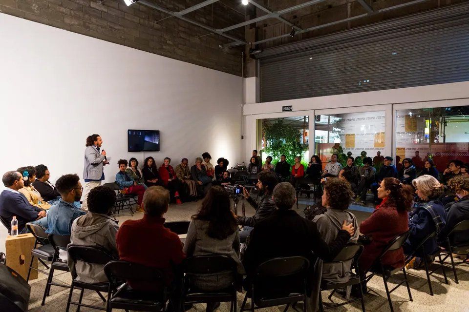 Um grupo de pessoas está sentado em cadeiras em uma sala assistindo a uma apresentação.