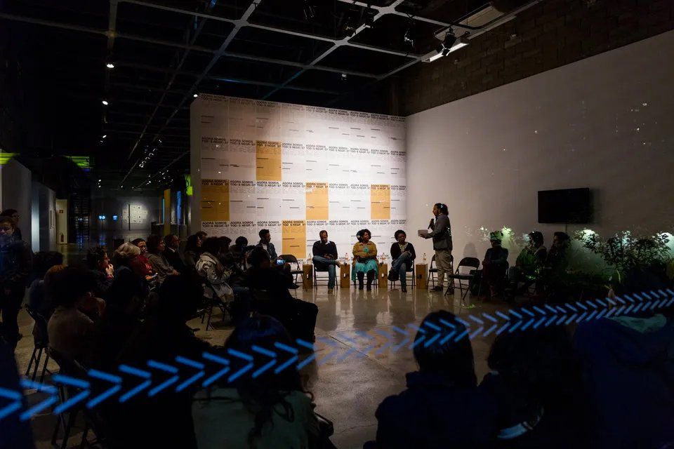 Um grupo de pessoas está sentado em cadeiras em uma sala escura.