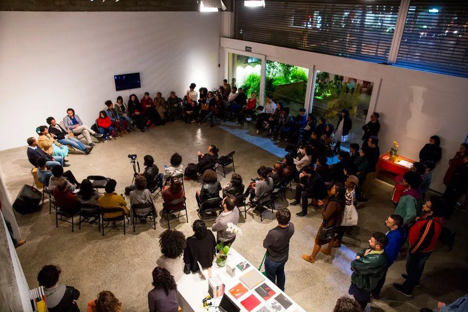 Um grupo de pessoas está sentado em círculo em uma sala.