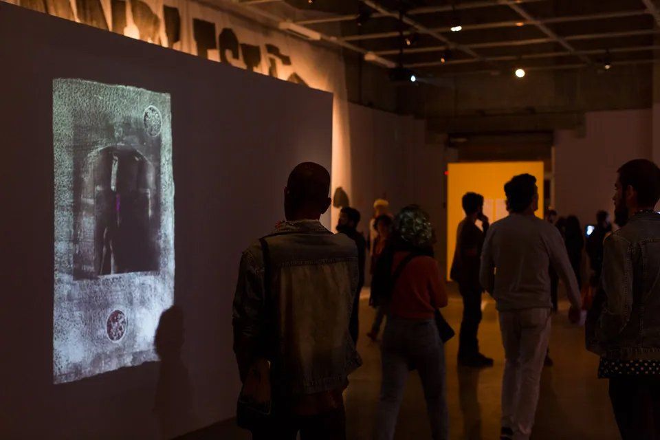 Um grupo de pessoas está em uma sala escura olhando para uma pintura na parede.