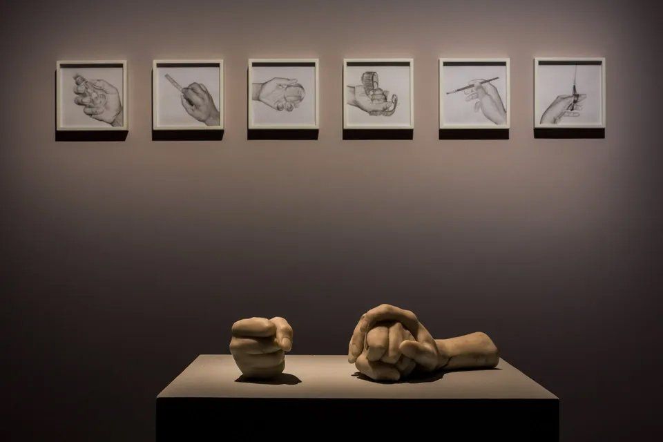 Uma estátua de um punho está sobre uma mesa em frente a uma parede com desenhos de mãos.