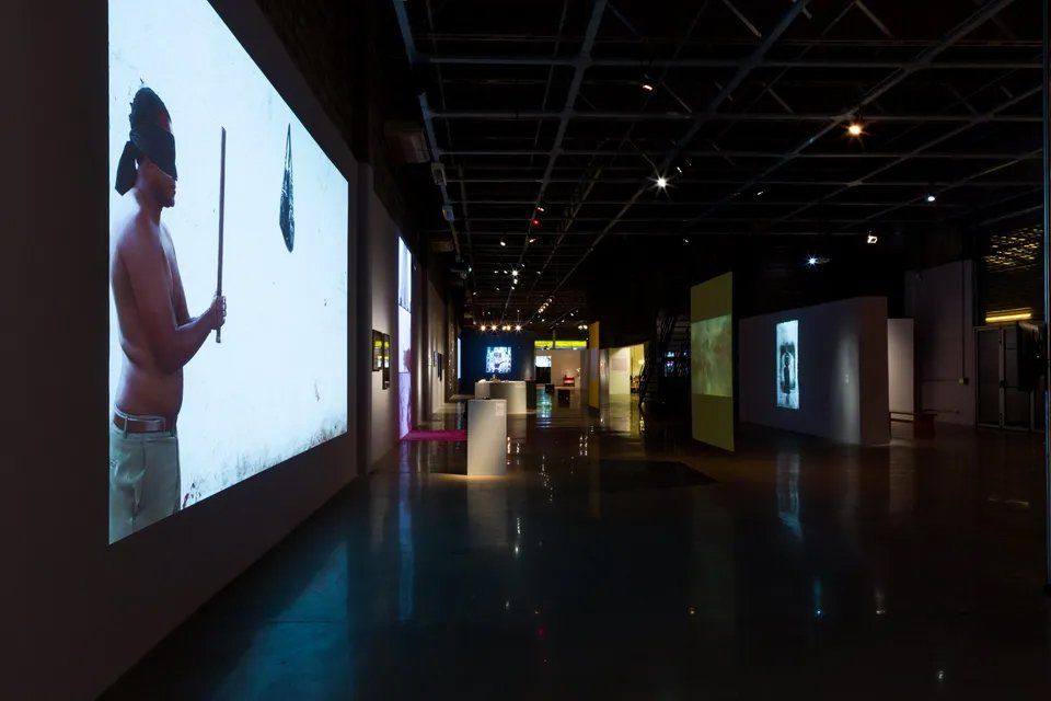 Um homem sem camisa está diante de uma grande tela em um quarto escuro.