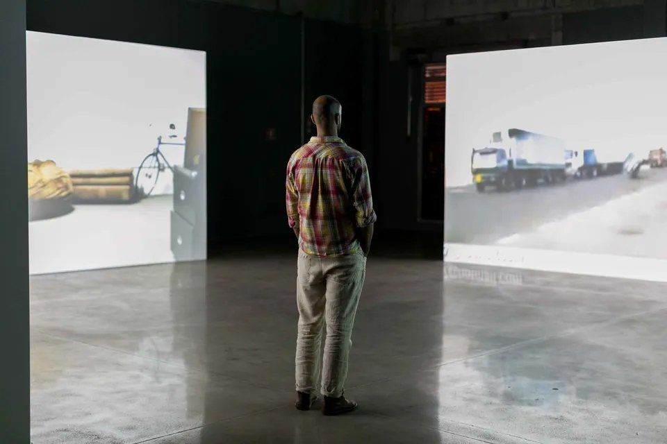 Um homem está diante de duas grandes telas em uma sala escura.