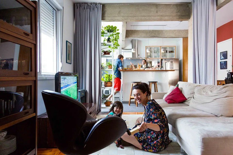 Uma mulher está sentada no chão de uma sala com dois filhos.