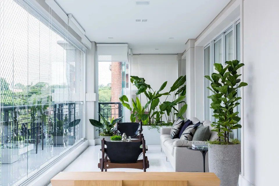 Uma varanda com sofá, cadeira, mesa e vasos de plantas.