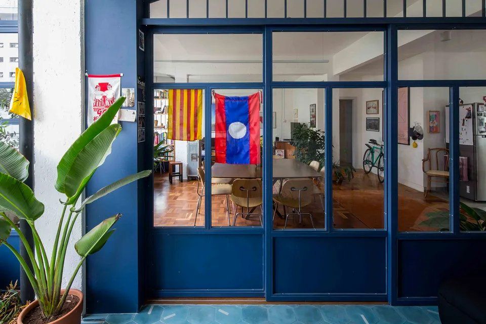 Uma porta azul está aberta para uma sala de estar com mesa e cadeiras.