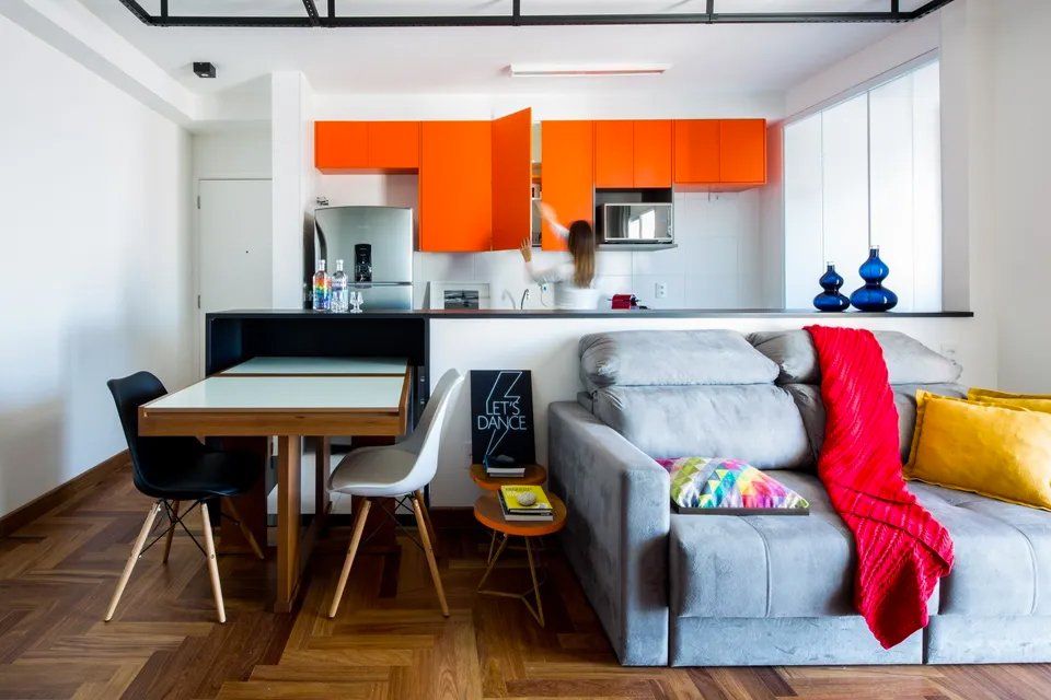 Uma sala com sofá, mesa, cadeiras e armários laranja.