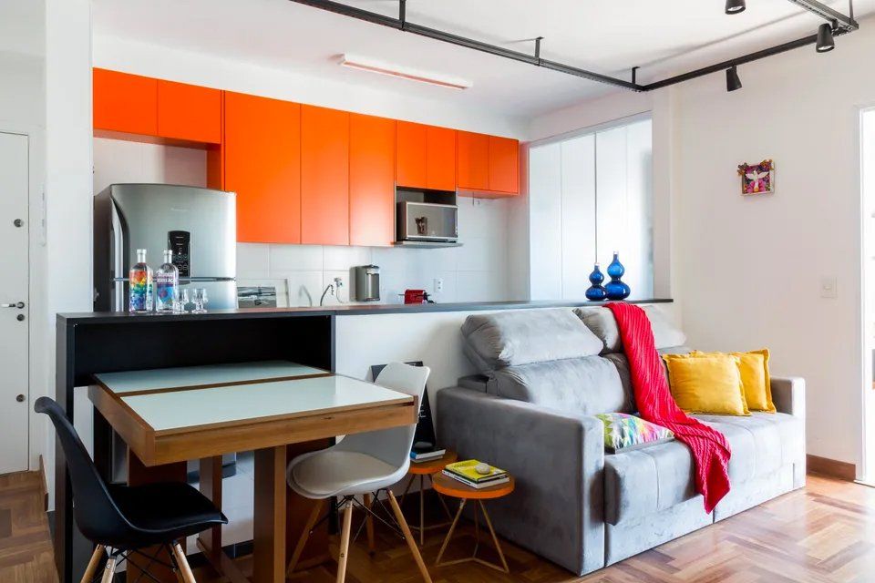 Uma sala com sofá, mesa, cadeiras e armários laranja.