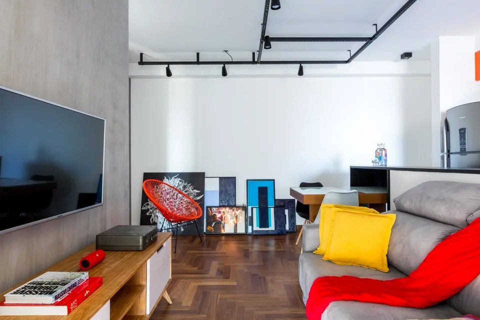 Uma sala de estar com sofá, televisão e pinturas na parede.