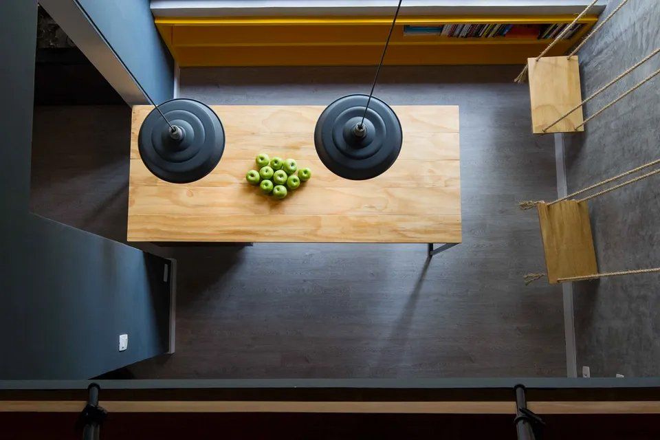 Uma vista aérea de uma cozinha com uma mesa de madeira e uma tigela de maçãs verdes.