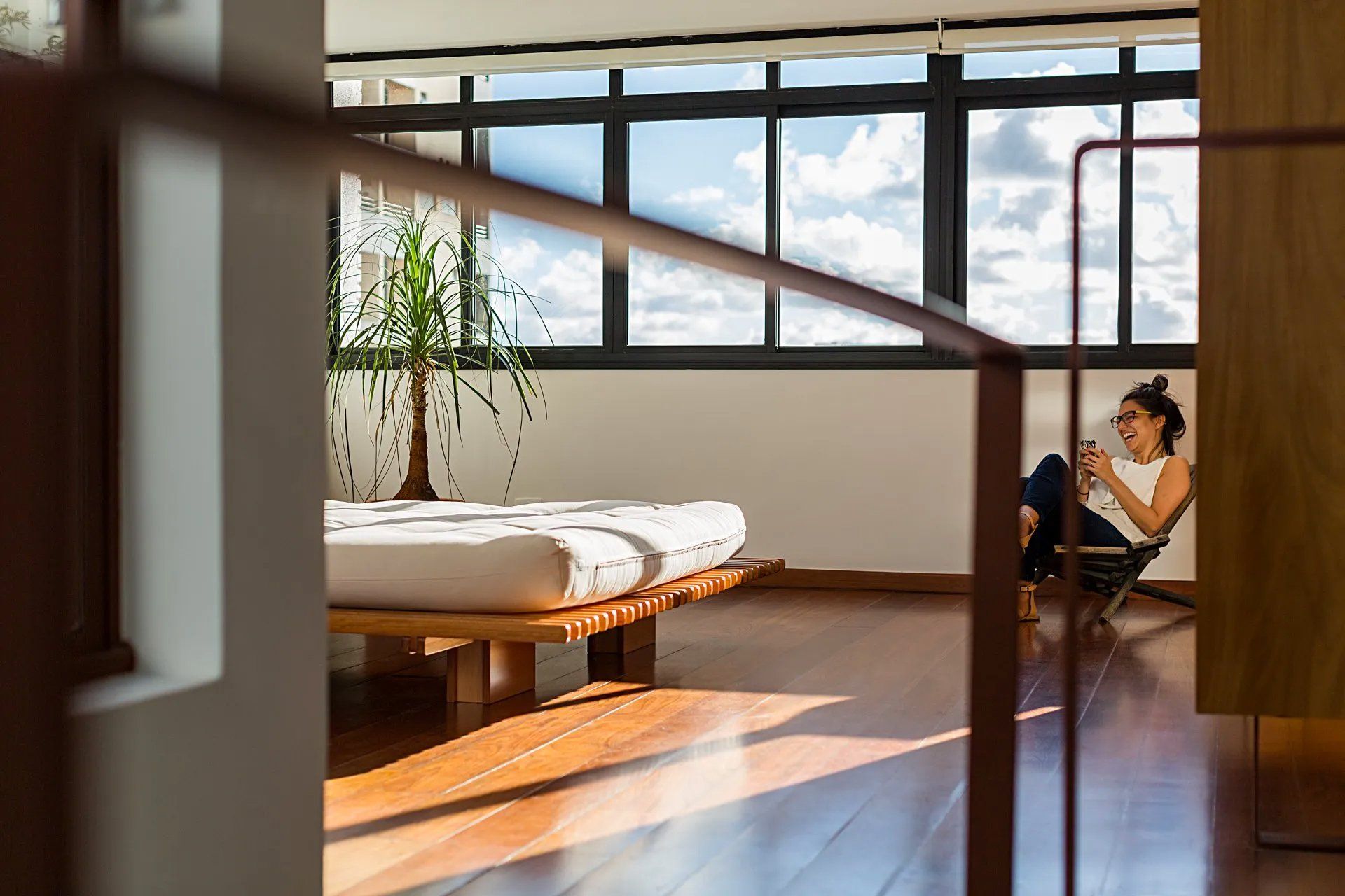 Uma mulher está sentada em uma cadeira em um quarto ao lado de uma cama.