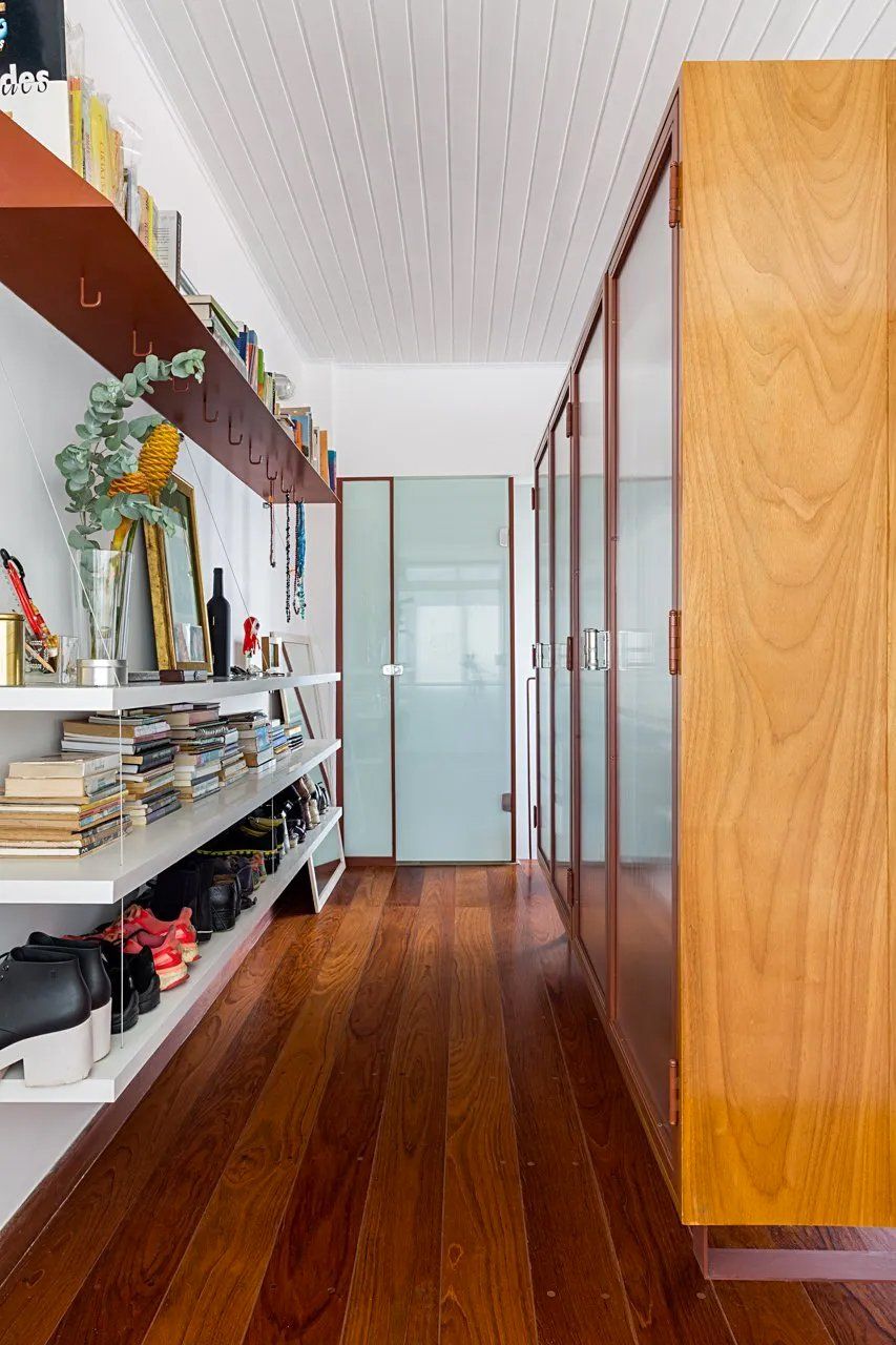 Um longo corredor com piso de madeira e prateleiras cheias de livros e sapatos.