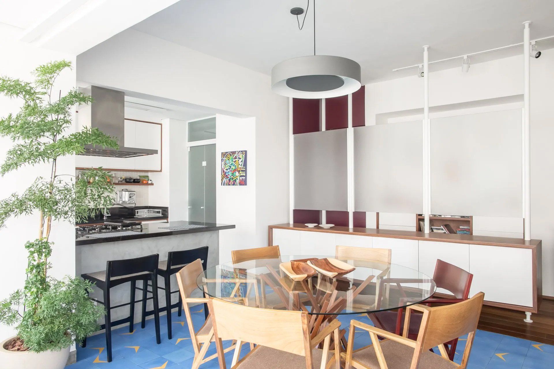 Uma sala de jantar com mesa e cadeiras de vidro e uma cozinha ao fundo.