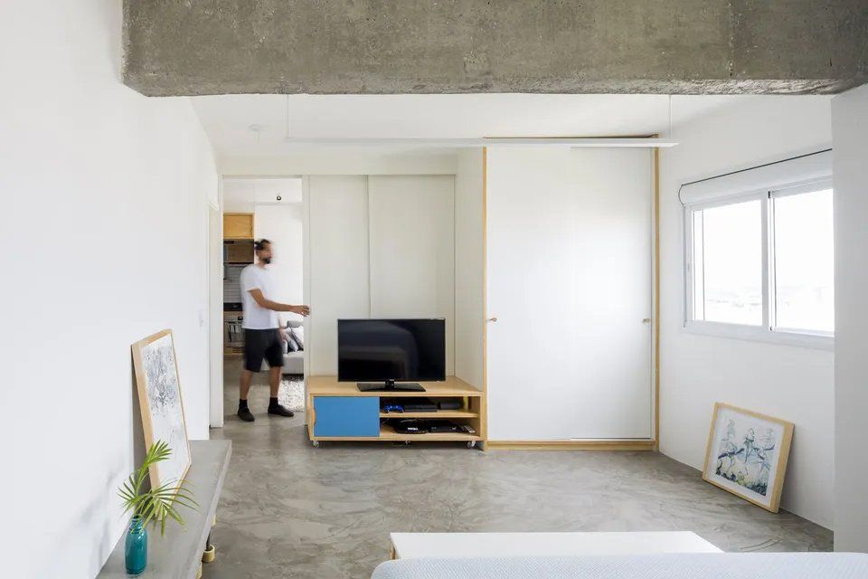 Um homem está parado em uma sala de estar ao lado de uma televisão.