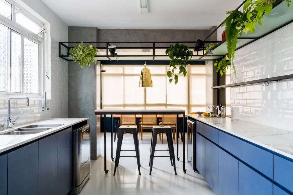 Uma cozinha com armários azuis, pia, mesa e banquetas.